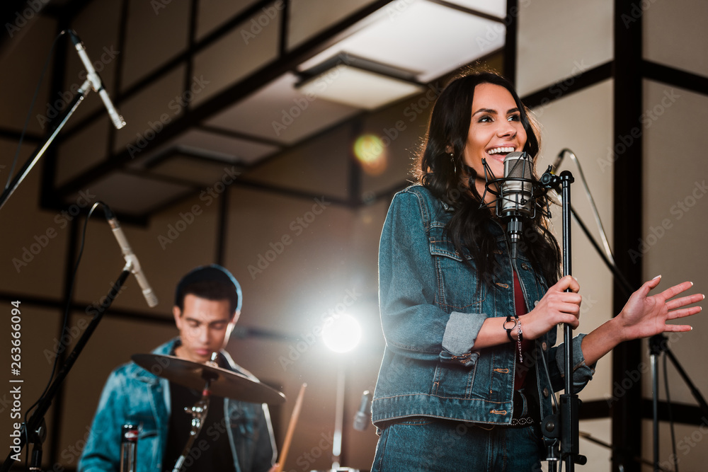 Fototapeta premium selective focus of excited woman singing in recording studio while handsome mixed race musician playing drums