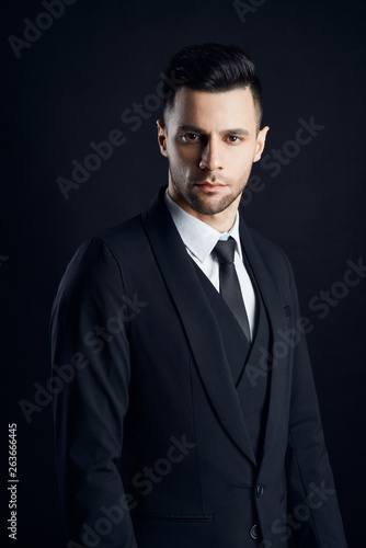 Handsome confident man in black suit on dark background