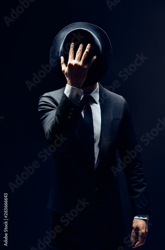Canvas Print Man in suit hiding face behind his hat isolated on dark background
