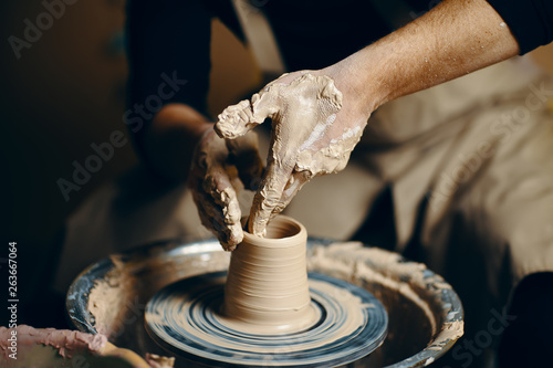 Man potter working on potters wheel making ceramic pot from clay in pottery workshop