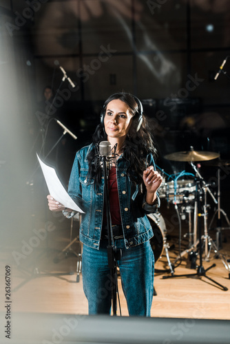 selective focus of inspired woman in headphones standing near microphone in recording studio © LIGHTFIELD STUDIOS