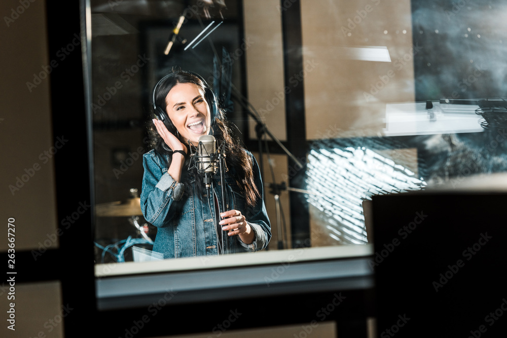 beautiful, inspired musician singing near microphone in recording studio