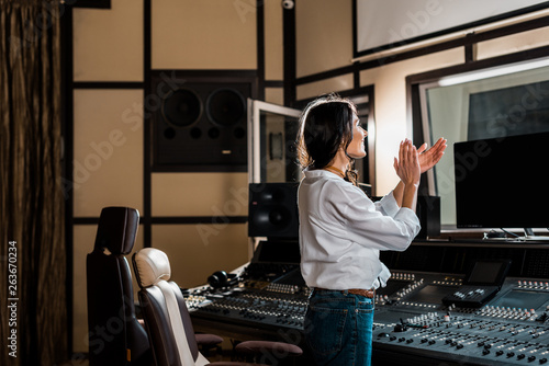 attractive sound producer applauding in recording studio near mixing console photo