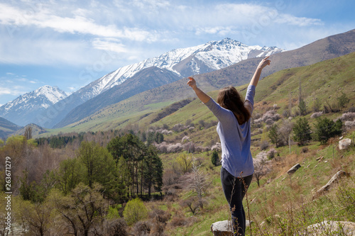 Young girl traveler on the background of spring mountains with their hands up. Nature and adventure.