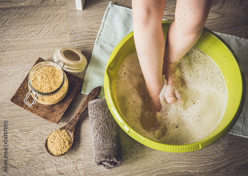 Foto Child taking a healing warming foot bath with mustard powder, adding mustard powder to foot bath with wooden spoon