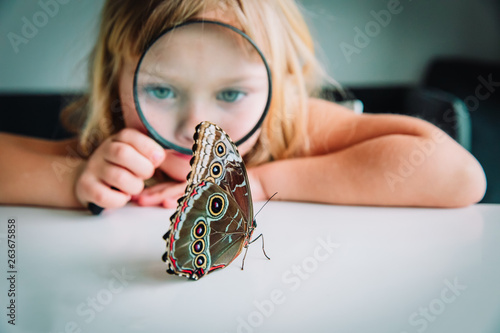 Little girl looking at butterfy through magnifying glass photo