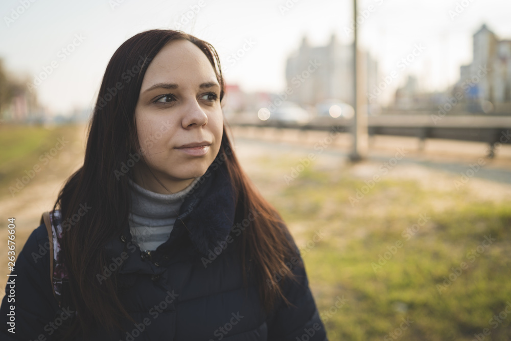 Young woman on city roadside Casual brunette in warm jacket standing on pavement of city roadway looking pensively away Young woman on city roadside Casual brunette in warm jacket standing on pavement of city roadway looking pensively away