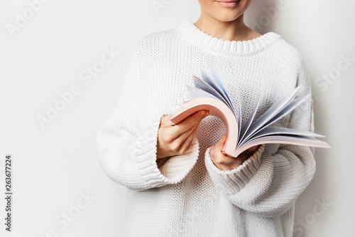 Close view of woman in white woolen sweater holding an open book with pink cover in hands. Mock up of Reading book concept background. photo