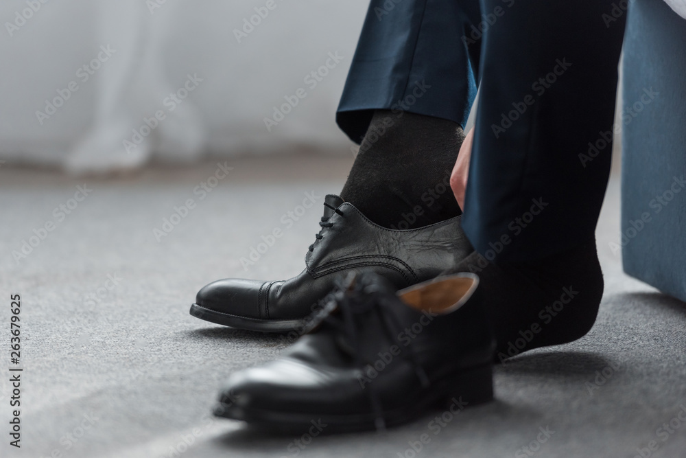 cropped view of man wearing black shoe at home