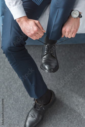 cropped view of man tying shoelaces on black shoes at home