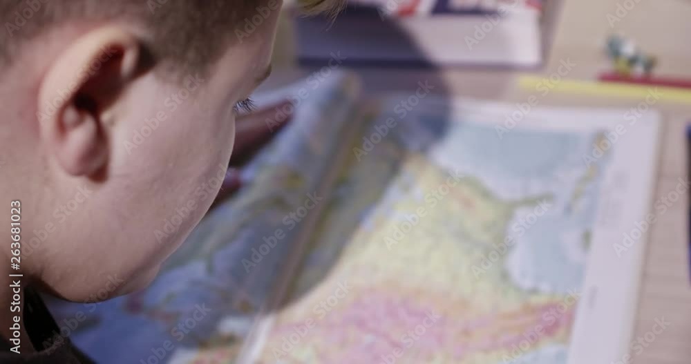 Young boy learning geography; he looks at the map; scans the area with his finger. Young boy learning geography; he looks at the map; scans the area with his finger.