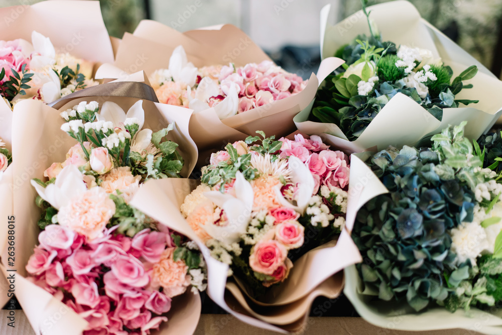 A lot of flower bouquets at the florist shop on the table made of hydrangea, roses, peonies, statice, eustoma in pink and sea green colors