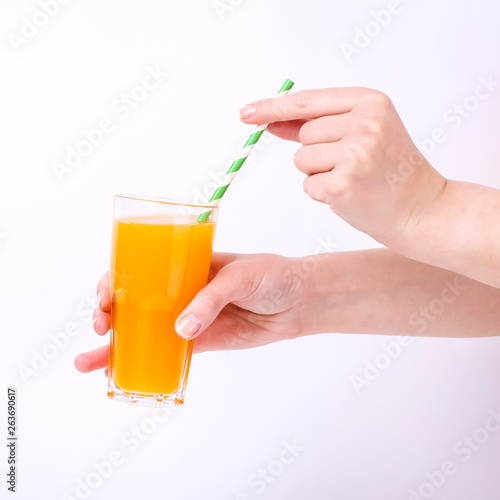 A glass with orange juice and a straw in hand in the girls. Isolate on white background.