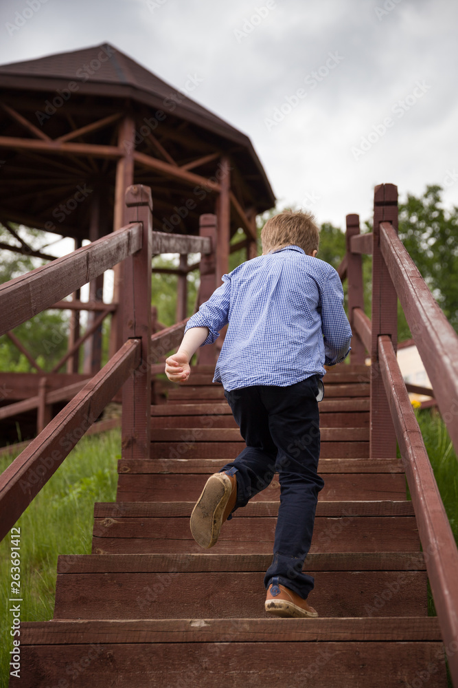The view from the back of the boy runs along the wooden stairs in the park. Cloudy, the child rushes into the arbor to shelter from the rain. Spring in the park The view from the back of the boy runs along the wooden stairs in the park. Cloudy, the child rushes into the arbor to shelter from the rain. Spring in the park