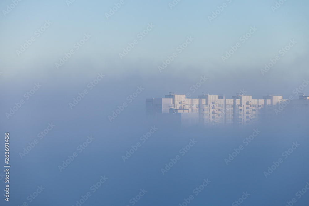 A lonely tall building peeking out from under a dense layer of fog that covered the city in the early morning. City concept. City in the clouds.