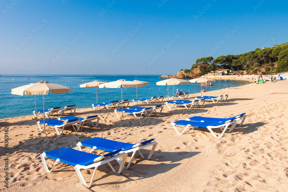 Cala de Fenals beach in Lloret de Mar, Costa Brava. Sandy resort beach in Spain with deck chairs and sun umbrella
