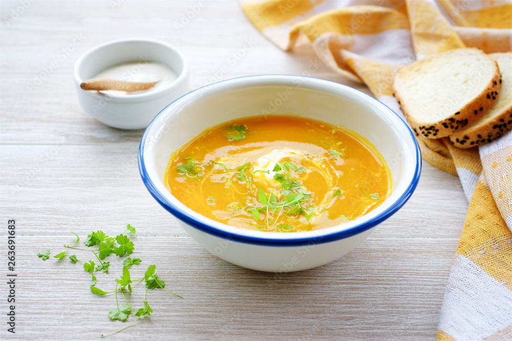 Pumpkin soup in white bowl with cream and parsley. Light wooden background Pumpkin soup in white bowl with cream and parsley. Light wooden background
