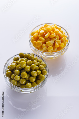 canned corn and green peas in a glass bowl on a white background