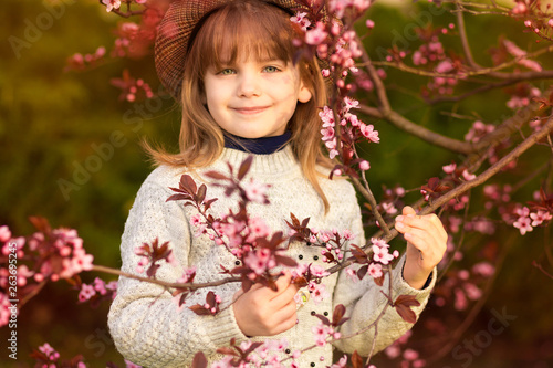 Spring portrait, adorable little girl in hat walk in blossom tree garden on sunset