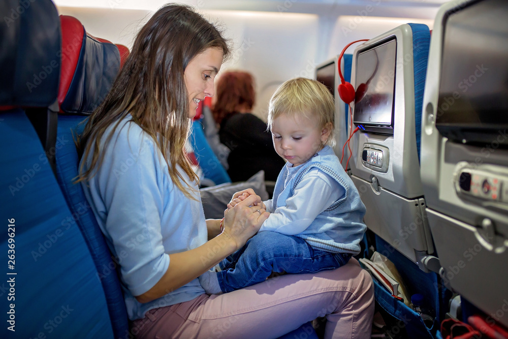 Mother, entertaining little toddler boy on board of aircraft on a long distance international flight Mother, entertaining little toddler boy on board of aircraft on a long distance international flight