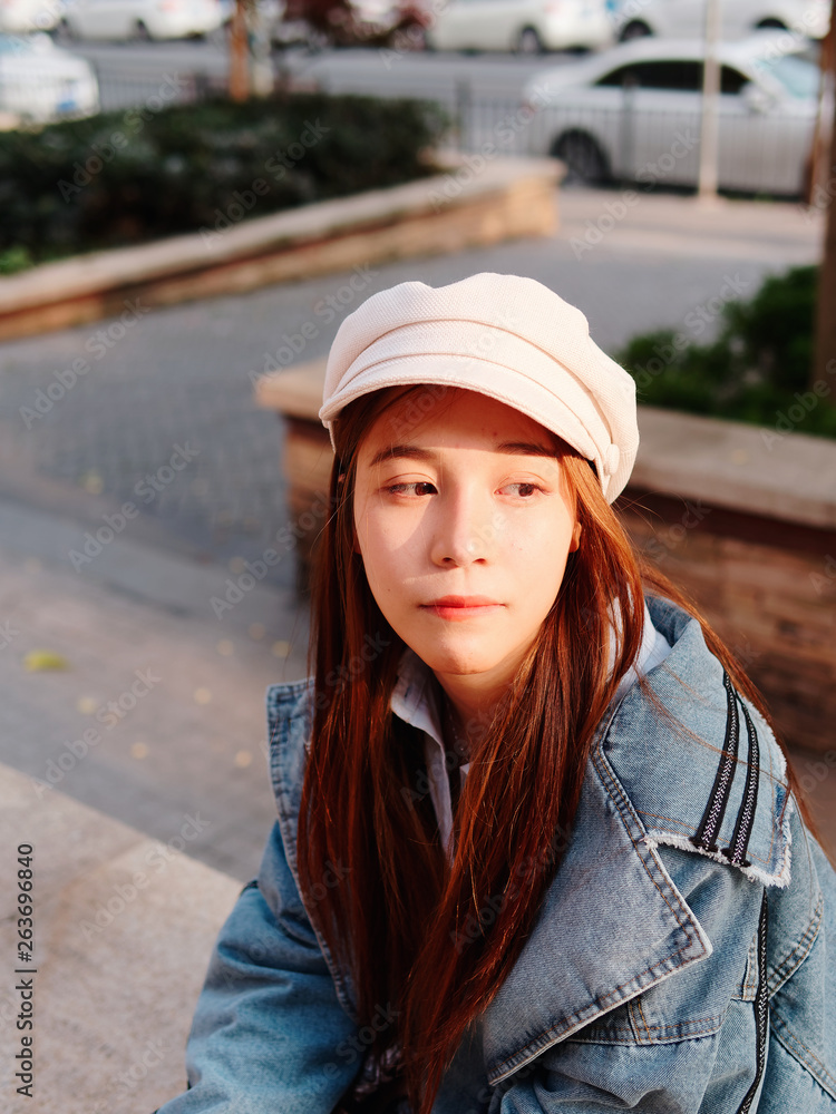 Street photography of a cute Chinese young woman in jeans and white hat with blur street background, female portrait.