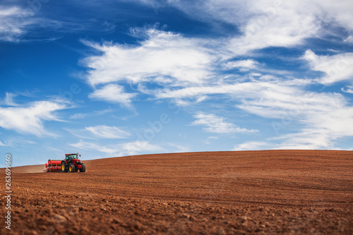 Farmer with tractor seeding crops at field