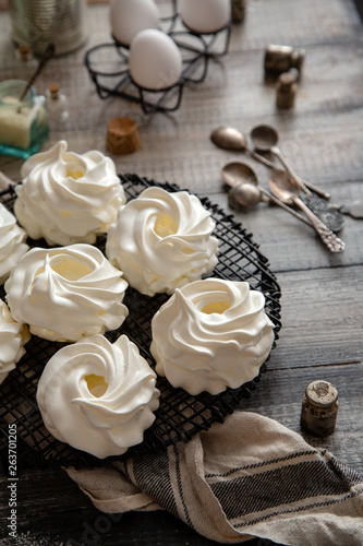 Homemade white mini meringue desserts pavlova on Wicker metal stand on grey wooden table 