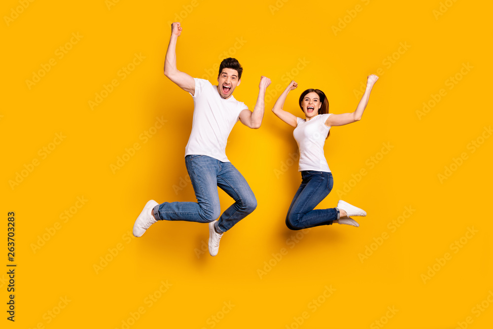 Full length body size photo funky she her he him his pair jumping high raised fists yell scream shout loud cheerleader football fans wear casual jeans denim white t-shirts isolated yellow background Full length body size photo funky she her he him his pair jumping high raised fists yell scream shout loud cheerleader football fans wear casual jeans denim white t-shirts isolated yellow background