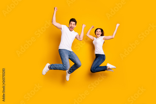 Full length body size photo funky she her he him his pair jumping high raised fists yell scream shout loud cheerleader football fans wear casual jeans denim white t-shirts isolated yellow background