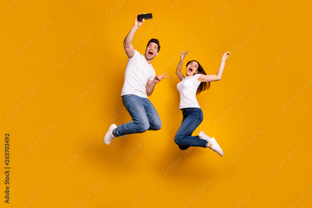Full length side profile body size photo funky funny two people she her he him his guy lady jump high show v-sign make take selfies wear casual jeans denim white t-shirts isolated yellow background