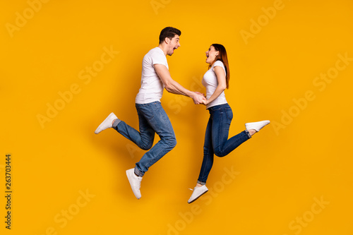Full length side profile body size photo funky crazy she her he him his pair touch arms jumping high yell scream shout best buddies wear casual jeans denim white t-shirts isolated yellow background