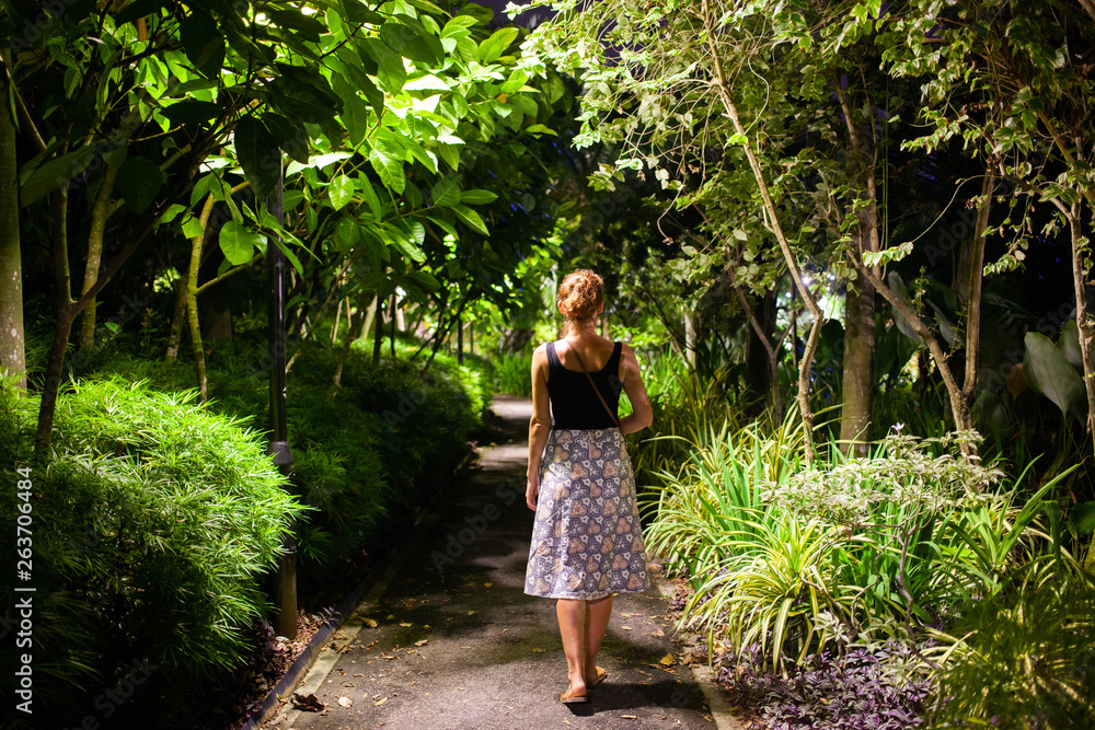 woman walking in a park with tropical trees at night