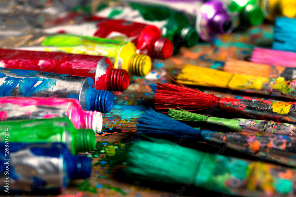 Fototapeta premium Stained paintbrushes and acrylic pain tubes on artist table. Artistic background