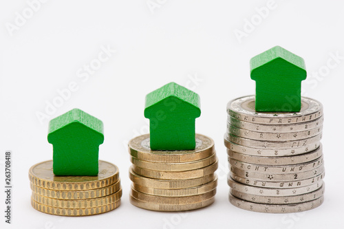 Trois piles de pièces de monnaie en euro, surmontées de petites maisons vertes en forme de flèches pointées vers le haut, fond blanc photo