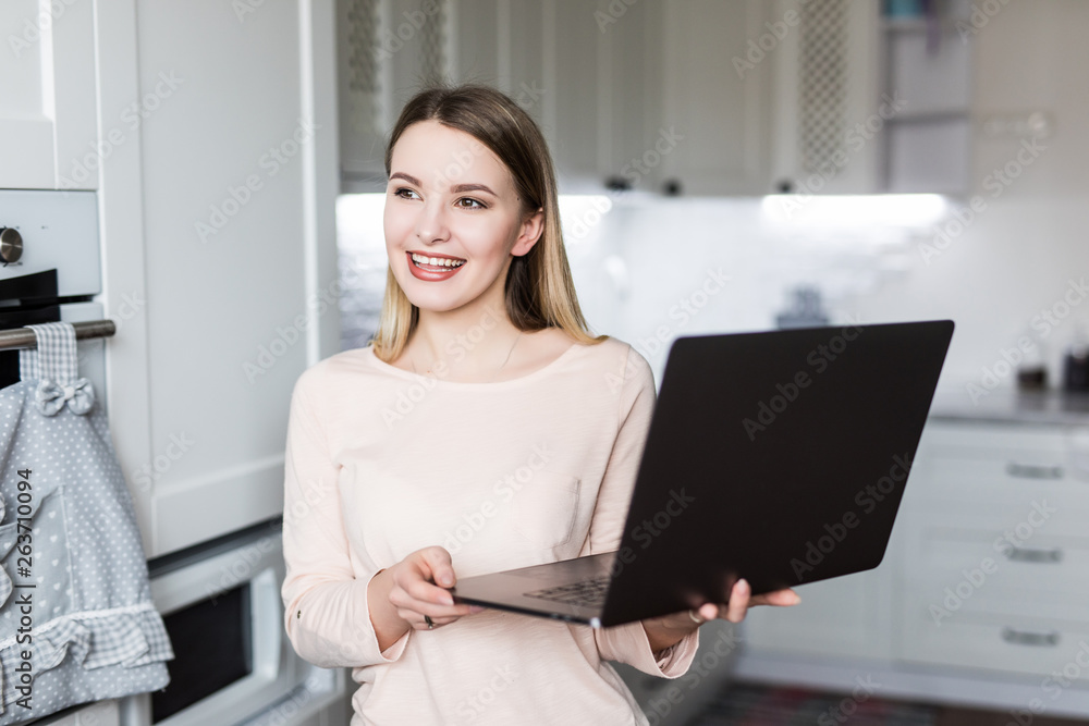 Charming blonde woman with a laptop looking into the camera in the kitchen Charming blonde woman with a laptop looking into the camera in the kitchen