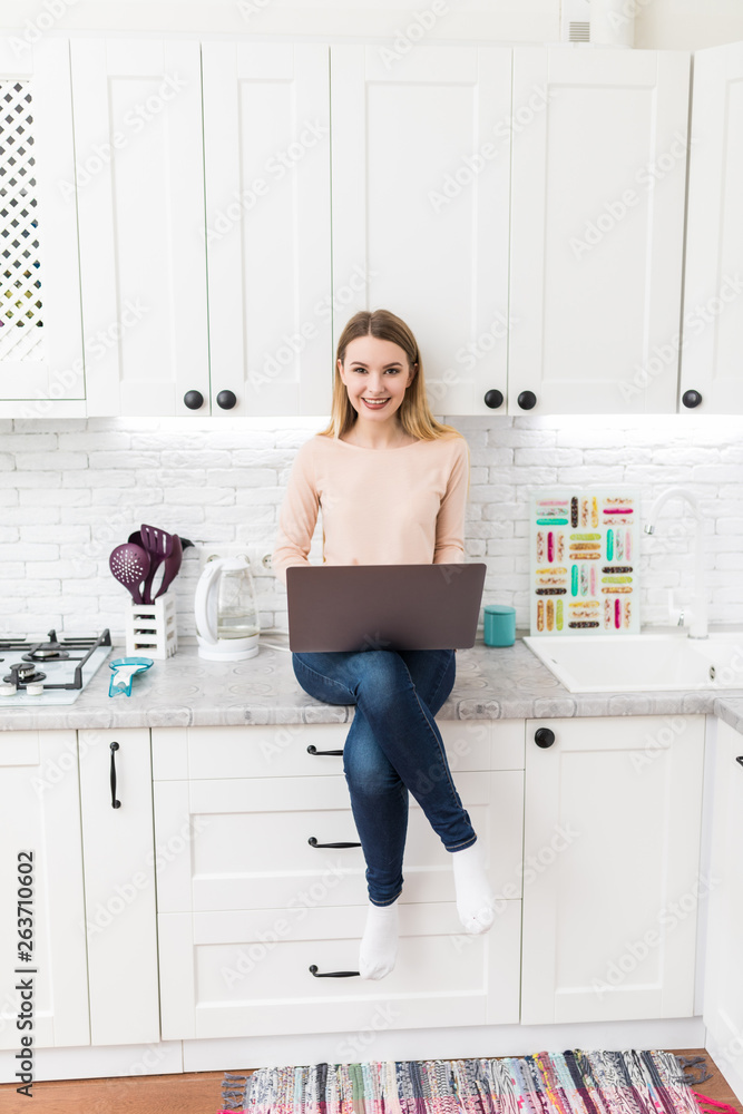 Young Woman in kitchen with laptop computer looking recipes, smiling. Food blogger concept Young Woman in kitchen with laptop computer looking recipes, smiling. Food blogger concept