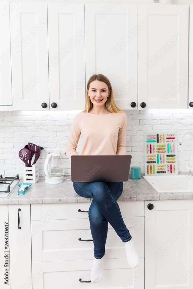 Young Woman in kitchen with laptop computer looking recipes, smiling. Food blogger concept Young Woman in kitchen with laptop computer looking recipes, smiling. Food blogger concept