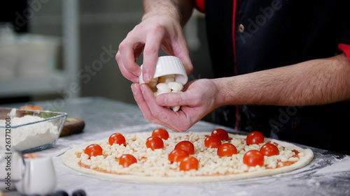 Restaurant kitchen. A chef putting special cheese on the pizza