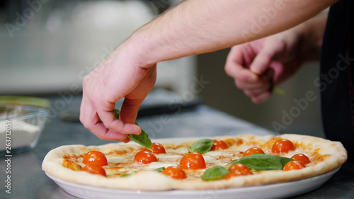 Restaurant kitchen. A chef decorating the pizza with greenery