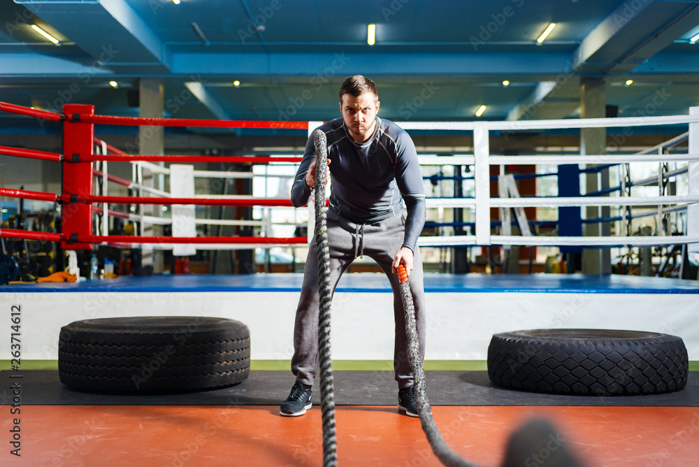 Obraz premium young guy trains strength fitness. man doing strength exercise with ropes.