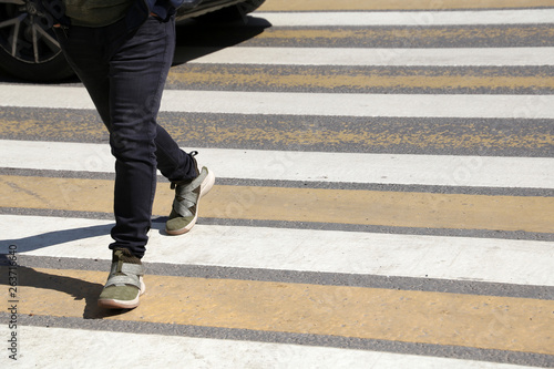 Pedestrian crossing the road at a crosswalk in front of the car. Man walking on zebra marking, male legs on the street, traffic violation and accident concept