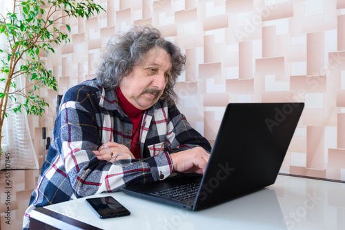 A happy smiling elderly man at the laptop sitting at the table at home.