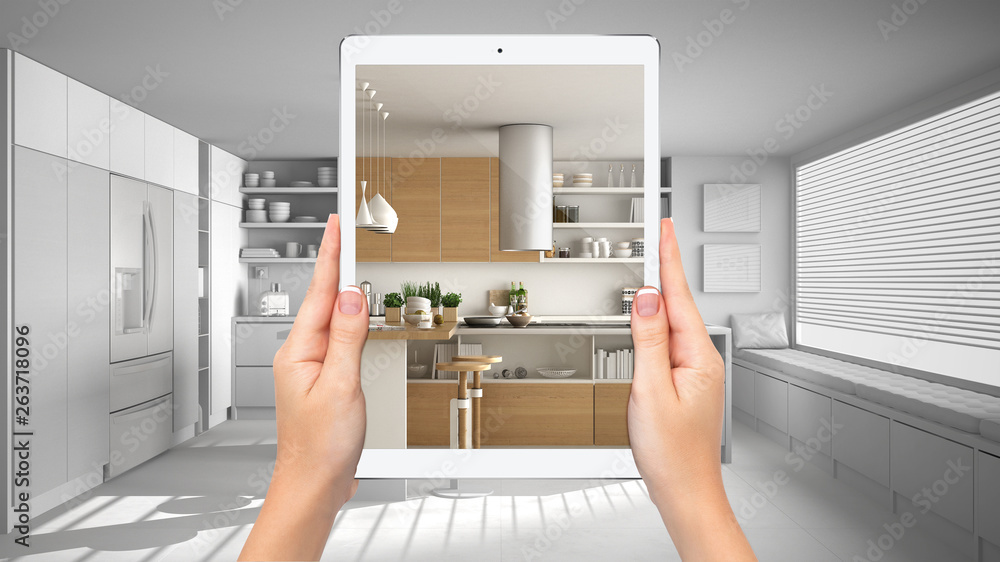 Hands holding tablet showing modern white and wooden kitchen, total blank project background, augmented reality concept, application to simulate furniture and interior design products Hands holding tablet showing modern white and wooden kitchen, total blank project background, augmented reality concept, application to simulate furniture and interior design products