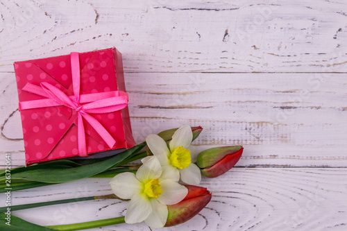 Fototapeta Naklejka Na Ścianę i Meble -  Gift box and bouquet of red tulips and daffodils on white wooden background. Concept of Valentine's Day, Women's Day, Mother's Day and Birthday. Top view, copy space
