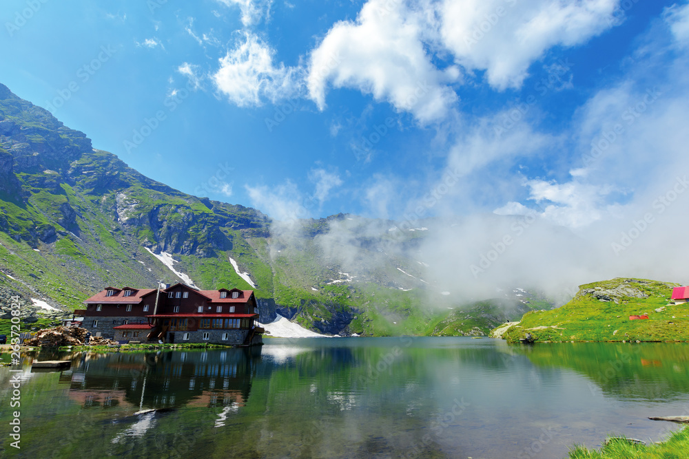 Fototapeta premium beautiful summer scenery around balea lake. grassy meadows and low clouds around. popular travel destination. location fagaras mountains, romania, europe. wonderful sunny weather