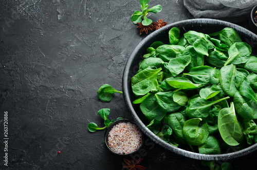 Fresh spinach. In a black plate on a wooden background Top view. Free space for your text. Flat lay
