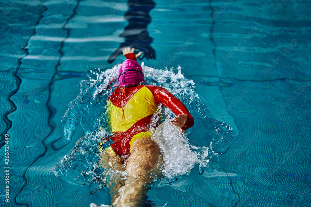Female athlete swimming fast in crawl style.  Splashes of water scatter in different directions.