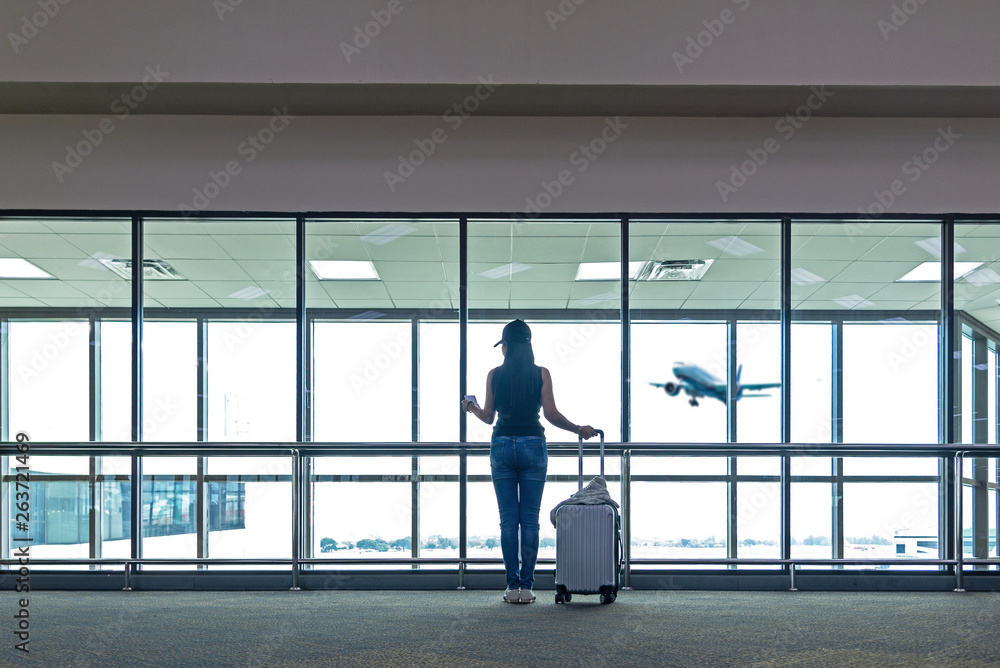 Fototapeta premium Traveler women plan and backpack see the airplane at the airport glass window, Asian tourist hold bag and waiting near luggage in hall airplane departure. Travel Vacation Concept.