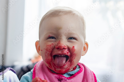 A small child eats fresh berries and smeared his face. Very funny image.