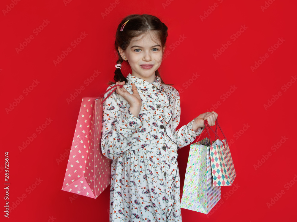 smiling young girl holding a gift bags in her hands on a red background, concept of advertising, sales, discounts smiling young girl holding a gift bags in her hands on a red background, concept of advertising, sales, discounts